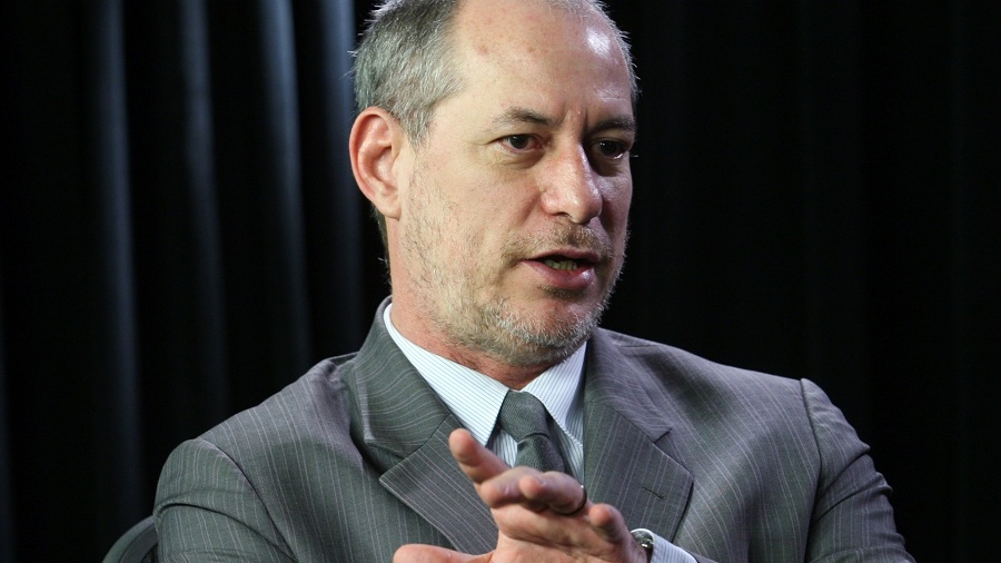 Ciro Gomes em evento, rodeado por pessoas, sorri. Ele usa terno e ao fundo, é possível ver parte da bandeira do Brasil - Metrópoles
