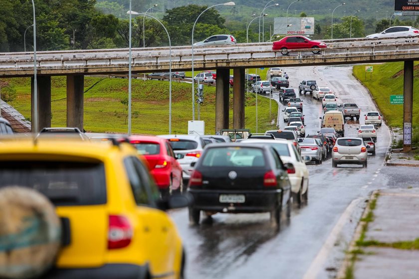 Carros trafegando em pista e viaduto ao fundo