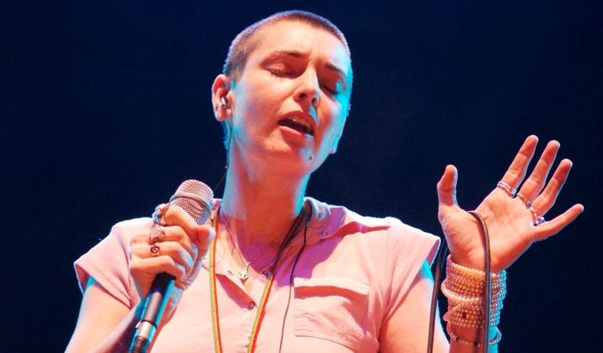 Foto colorida de Sinéad O'Connor cantando - Metrópoles