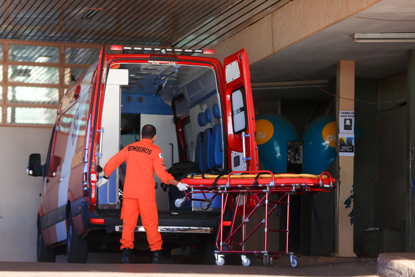 Bombeiro com mão em maca atrás de ambulância com portas abertas
