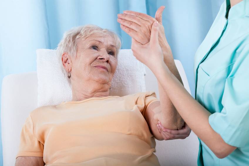Mulher de jaleco segura braço de senhora com osteoroporose deitada - Metrópoles