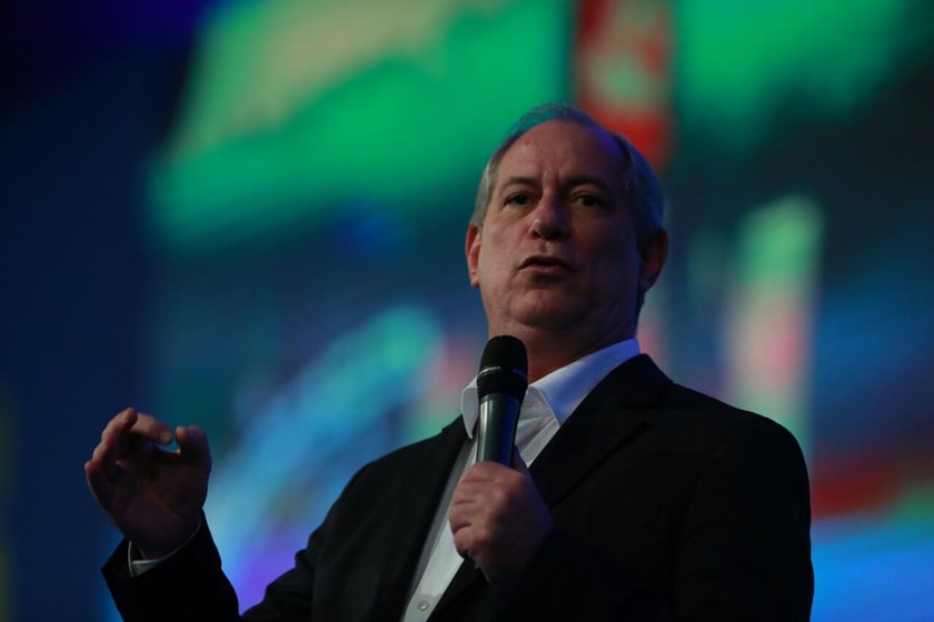 Sob painel florescente, ao fundo, Ciro Gomes fala no microfone para plateia. Ele usa terno e camisa social - Metrópoles