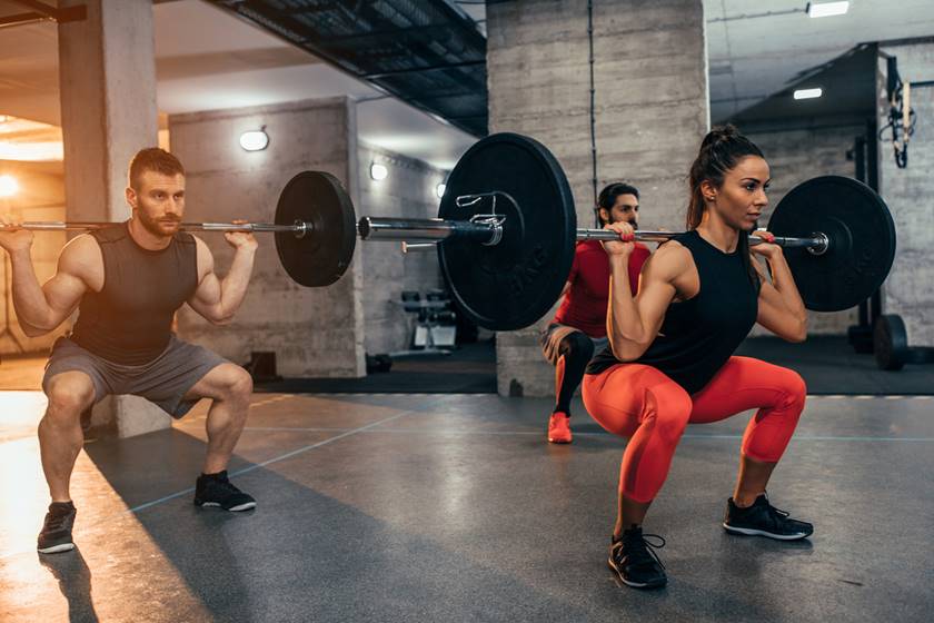 Imagem colorida de dois homem e uma mulher executando exercício de agachamento - Metrópoles