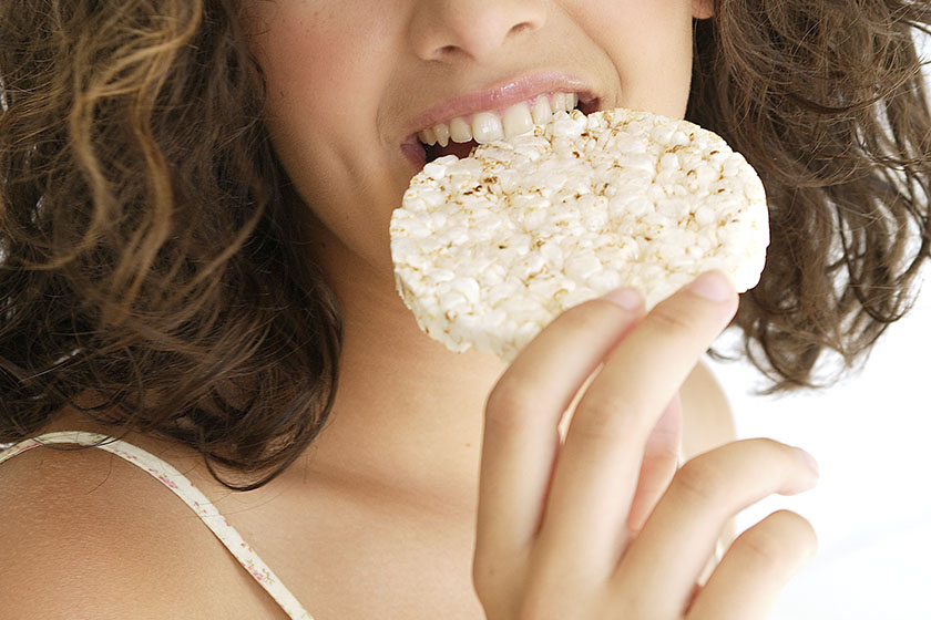 Imagem colorida mostra mulher mordendo um biscoito de arroz