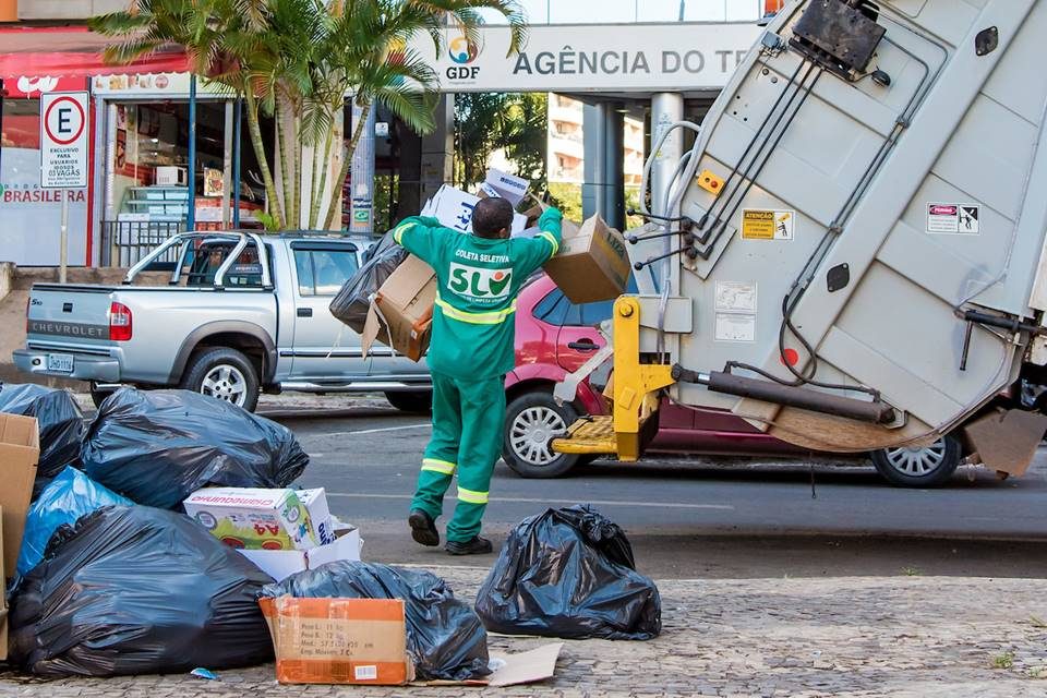 Trabalhador recolhendo lixo ao caminhão