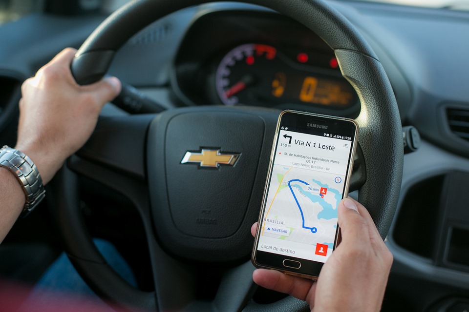 Motorista com a mão no volante e outra com o celular na mão