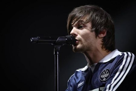 Foto colorida de Louis Tomlinson cantando em microfone - Metrópoles