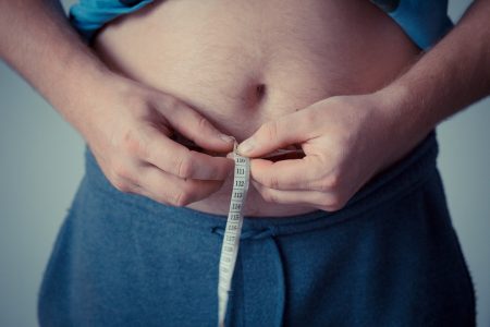 Imagem colorida de um homem medindo a própria barriga com uma fita métrica - Metrópoles