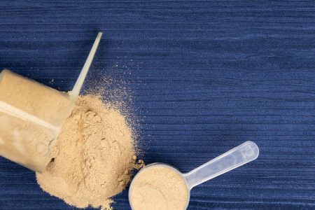 Foto colorida de scoop com suplemento alimentar derramado em mesa azul - Metrópoles