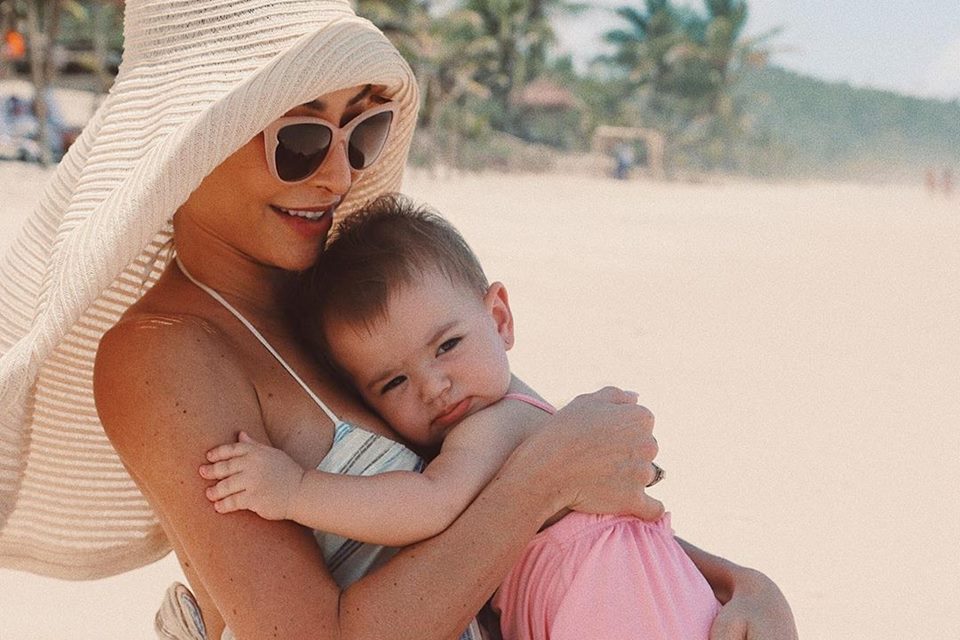 Sabrina com Zoe no colo, na beira da praia
