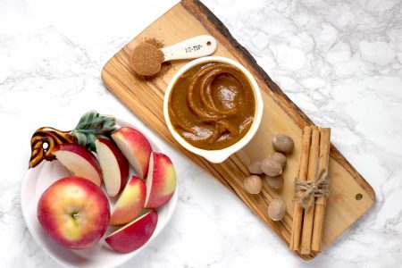 Foto colorida de uma vasilha com frutas e uma tábua de madeira com manteiga de amendoim