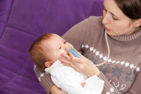 Bebê gripado com aparelho de desentupir o nariz no colo da mãe