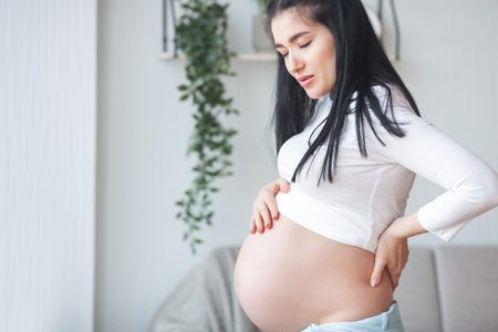 Mulher grávida com mão nas costas e passando mal