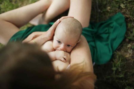 Imagem mostra mulher sentada e amamentando bebê, que olha para ela - Metrpopoles