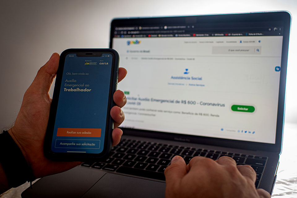 Aplicativo da caixa na mão do celular e computador ao fundo