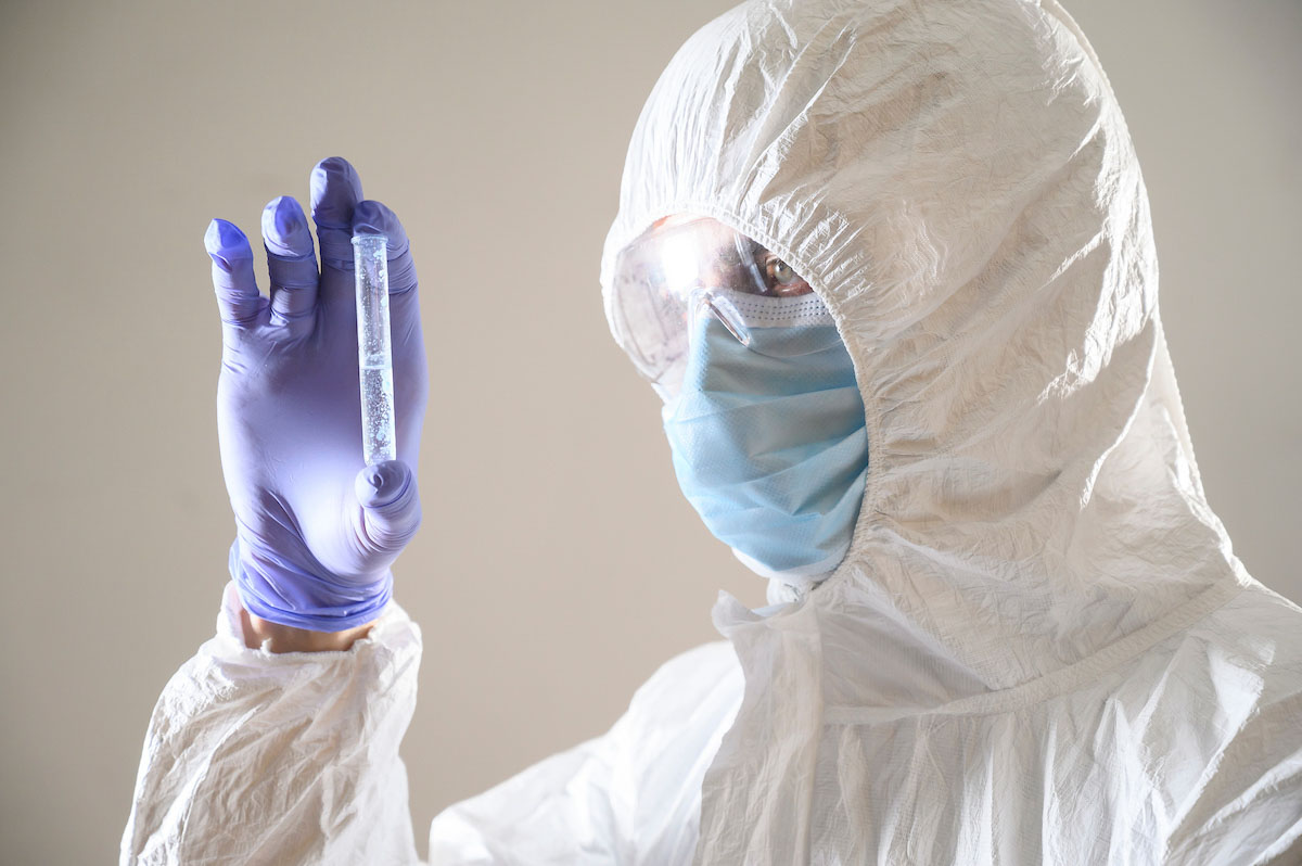 Cientista com mascara e EPI examina amostra de coronavirus