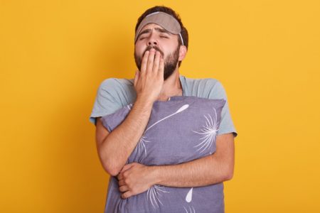 Homem aparentemente cansado agarrado a um travesseiro. Homem cansado bocejando - Metróples - hipersonia