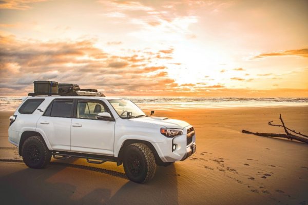 Carro estacionado em praia durante o por do sol, road trip