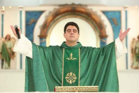 Fotografia colorida. Padre Robson aparece orando com os braços levantados para cima e os olhos fechados