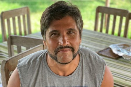 Leo Chaves de regata cinza sentado próximo a uma mesa - Metrópoles