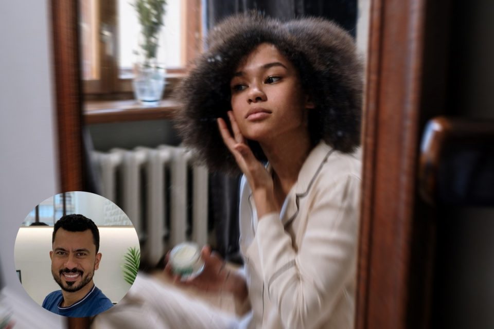 mulher negra passando produto no rosto de frente ao espelho