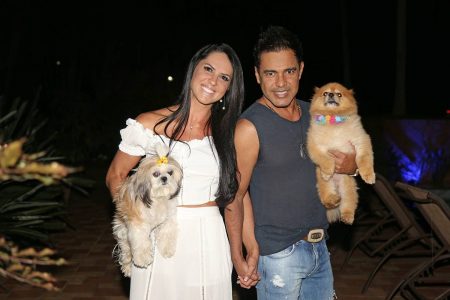 mulher de vestido branco de maos dadas com homem de camiseta cinza e cada um segura um cachorro no colo - Metrópoles