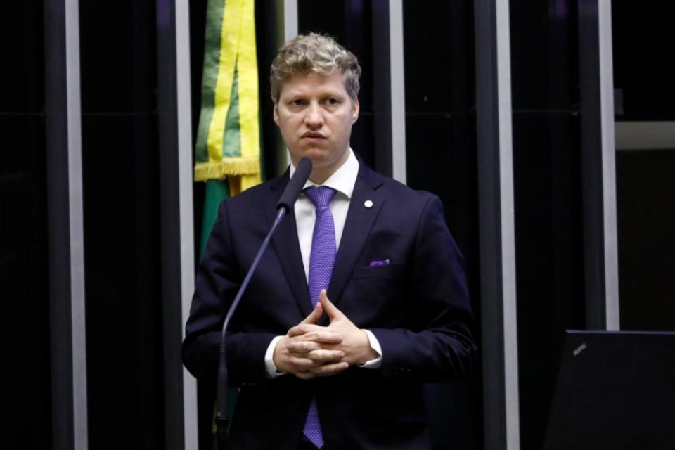 Novo O deputado do partido Novo pelo Rio Grande do Sul, Marcel van Hattem, discursa no plenário da Câmara dos Deputados diante de microfone. Ele está de mãos cruzadas - Metrópoles