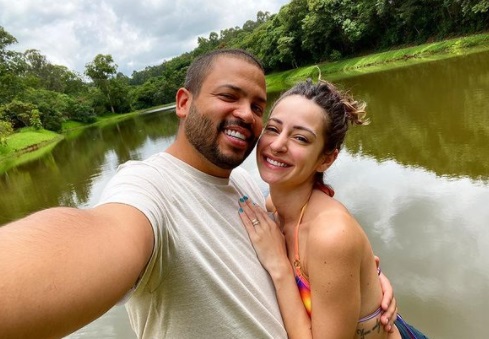 Projota e Tamy Contro. O cantor está de camisa clara, tem barba e está sorrindo. Tamy Contro está de roupa colorida, tem cabelos claros e também sorri - Metrópoles