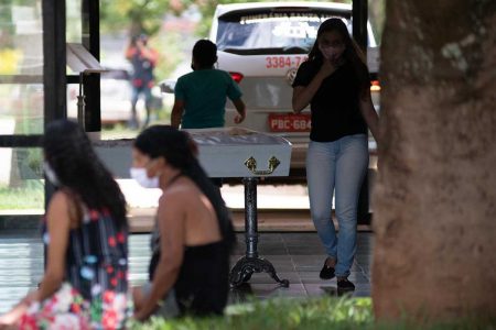 Homem e mulher de máscara ao lado de caixão de criança