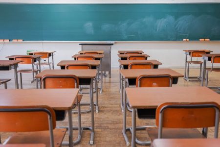 Fotografia colorida de carteiras enfileiradas em uma sala de aula vazia