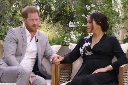 Príncipe Harry e Meghan Markle sentados em cadeiras de mãos dadas