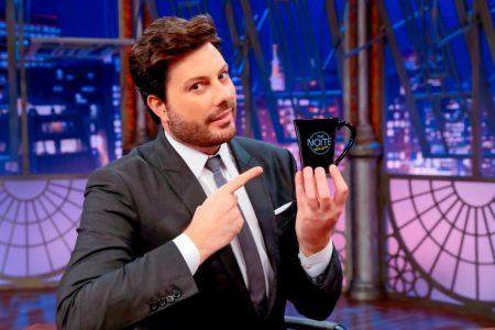 Danilo Gentili apresenta o programa The Noite. Ele usa terno e segura uma caneca preta - Metrópoles