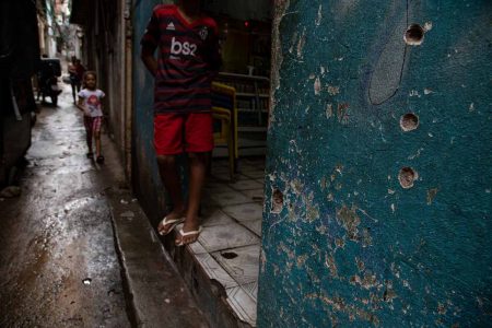 homem de bermuda e camiseta parado em beco com marcas de tiros no Jacarezinho