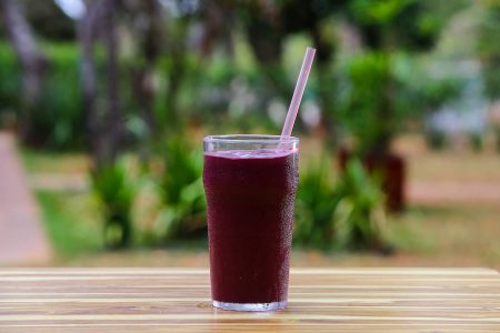 Copo com suco de uva e canudo de plástico em cima de mesa de madeira
