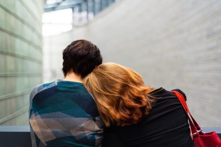 Imagem colorida de duas pessoas de costas, uma encostando a cabeça no outro - metrópoles