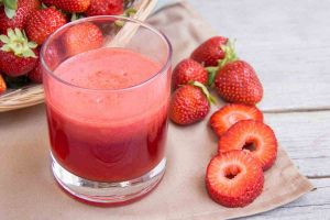 Imagem mostra morangos cortados ao lado de um copo de suco de morango de intensa cor vermelha - Metrópoles