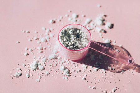 Foto colorida de medidor de suplemento alimentar em mesa cor de rosa - Metrópoles