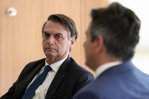 Bolsonaro, em segundo plano, olha para Ciro Nogueira, em primeiro plano e de costas, ambos sentados e de terno - Metrópoles