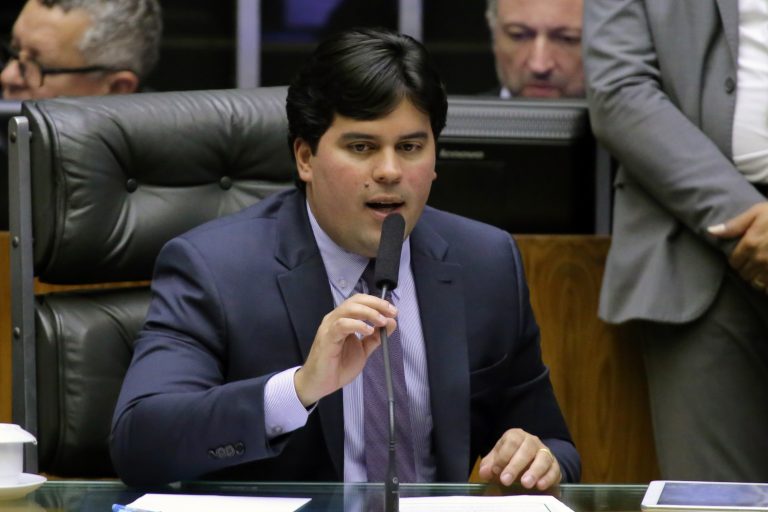 imagem mostra deputado andré fufuca segurando microfone. ele usa terno preto, camisa e gravata, tem os cabelos pretos lisos e pele branca