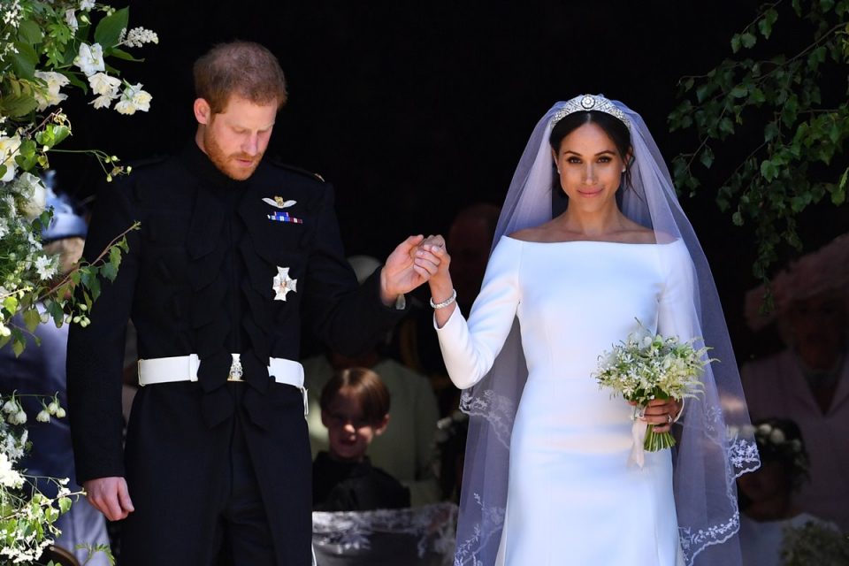 Foto colorida de homem ruivo, com traje militar preto, ao lado de mulher parda, com vestido de noiva, tiara, buquê e véu - Metrópoles