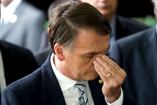 O presidente Jair Bolsonaro exibe semblante triste em evento, cercado por pessoas, com a mão no rosto e olho fechado - Metrópoles