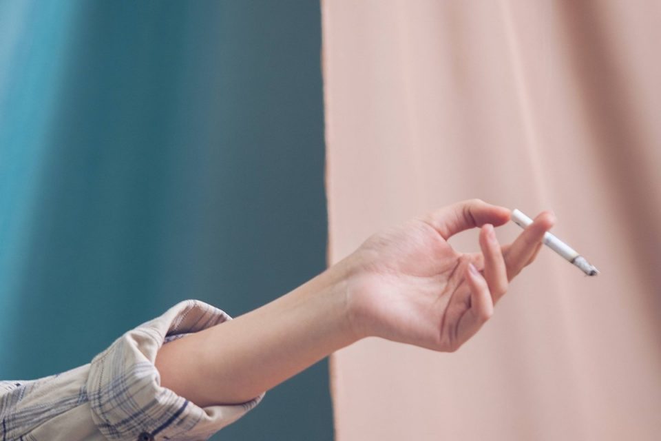 Imagem mostra mão em close de uma mulher segurando um cigarro. Conceito de tabagismo. Metrópoles