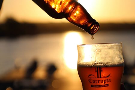 garrafa de cerveja derramando em copo com por do sol ao fundo