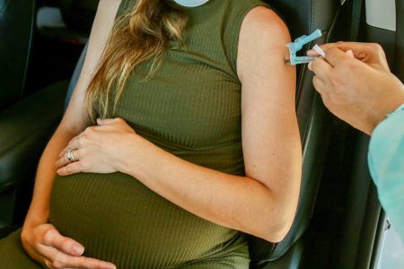 Mulher grávida com mão em barriga sendo vacinada no braço - Metrópoles