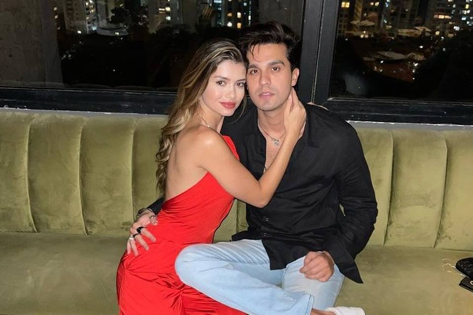 Foto colorida de Luan Santana e Izabela Cunha abraçados. Ela usa vestido vermelho, ele blusa preta e calça - Metrópoles