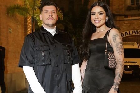 ferrugem de manga longa branca e blusa de botao preta ao lado da esposa, Thais, mulher de pele clara, cebelos longos escuros, que usa vestido preto - metrópoles
