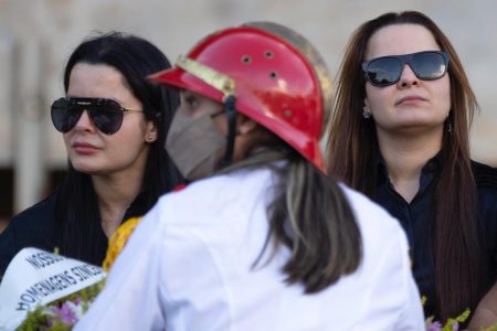 Mulher de branco de costas e, na frente delas, dias mulheres de óculos escuros