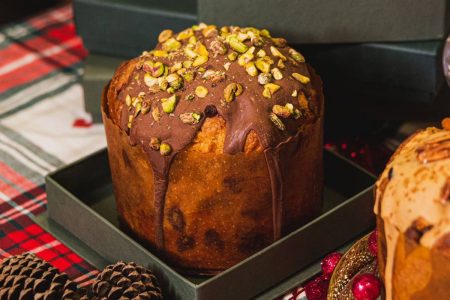 Na foto temos uma caixa preta com um panetone coberto com chocolate e pistache