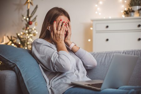 Mulher com a mão na cabeça e ansiosa com a época do ano. Casa dela está enfeitada para o natal