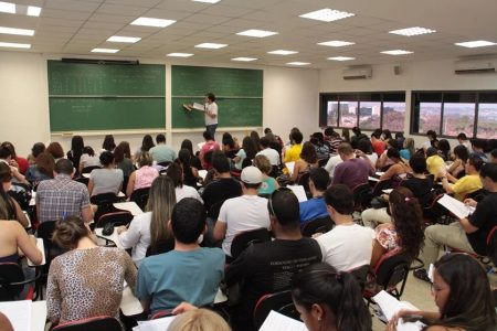 Fotografia colorida de sala de aula cheia de alunos com professor ao fundo